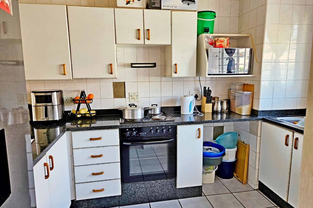 A functional kitchen featuring white cabinetry, granite countertops, a built-in oven, and tiled finishes throughout.