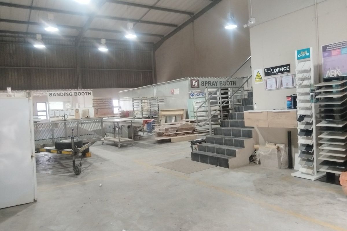 Spacious industrial workshop area featuring concrete flooring, high-clearance metal roof structure, dedicated spray and sanding booths, and an integrated office staircase.