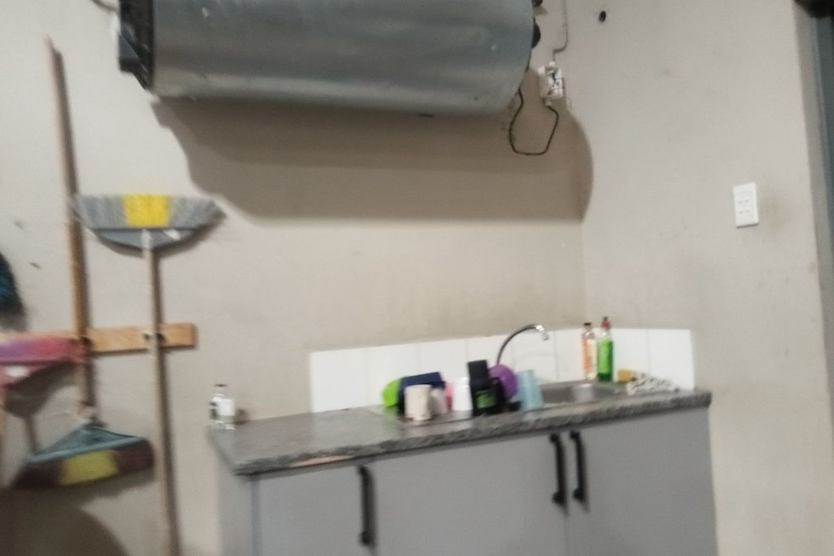 A functional laundry area featuring a wall-mounted electric water heater, sink, and built-in cabinetry with tiled splashback.