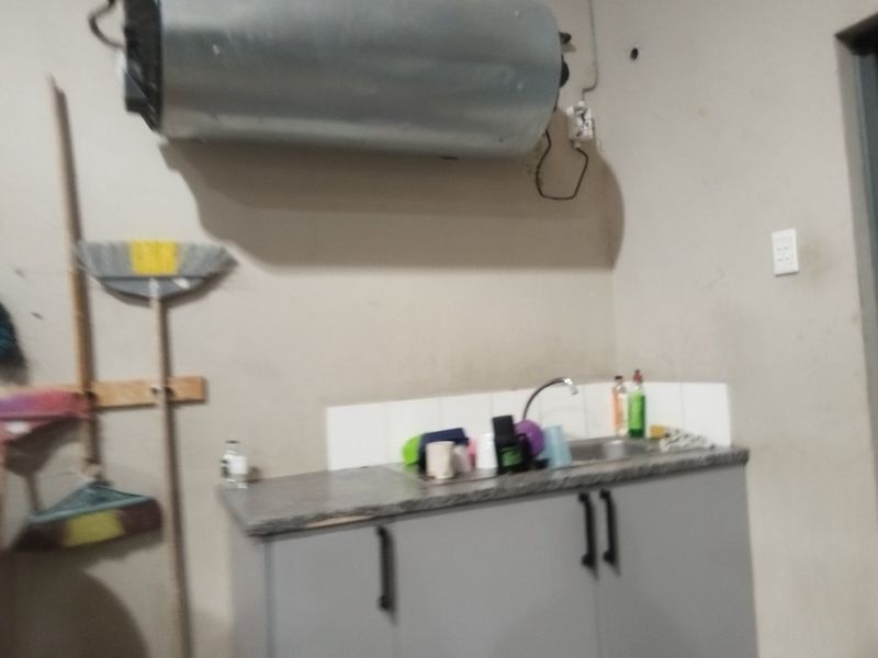 A functional laundry area featuring a wall-mounted electric water heater, sink, and built-in cabinetry with tiled splashback.