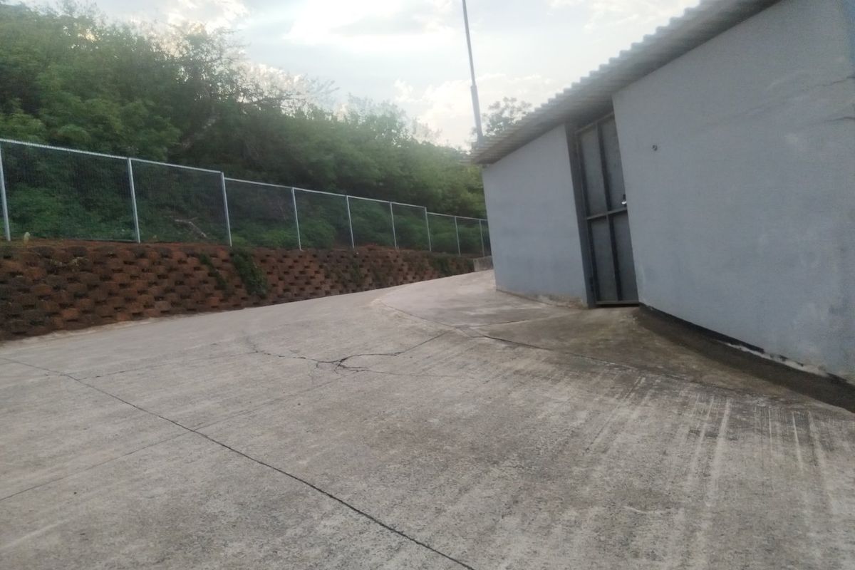 Exterior rear view of the industrial property featuring a concrete driveway, retaining wall, and perimeter wire mesh fencing.