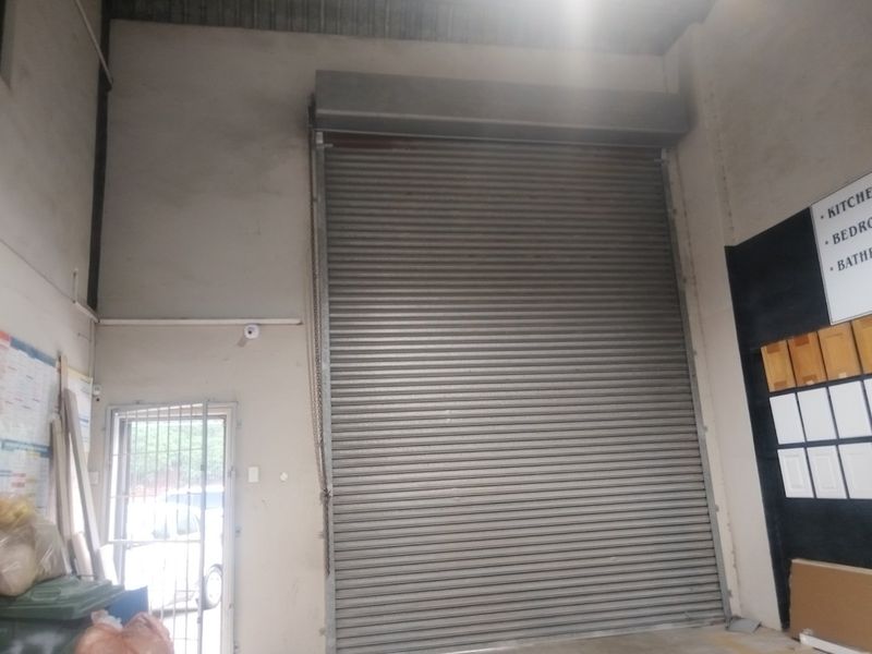 Industrial warehouse space featuring a large roller shutter door, high ceilings, and a secure pedestrian entrance gate.