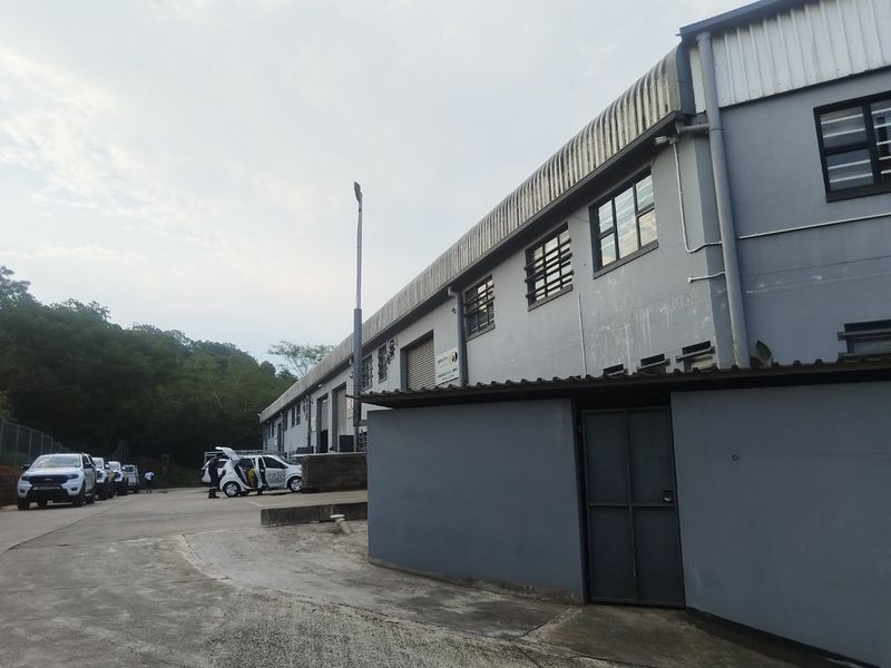 Exterior view of an industrial warehouse facility featuring metal cladding, roller shutter access, and a concrete driveway area.