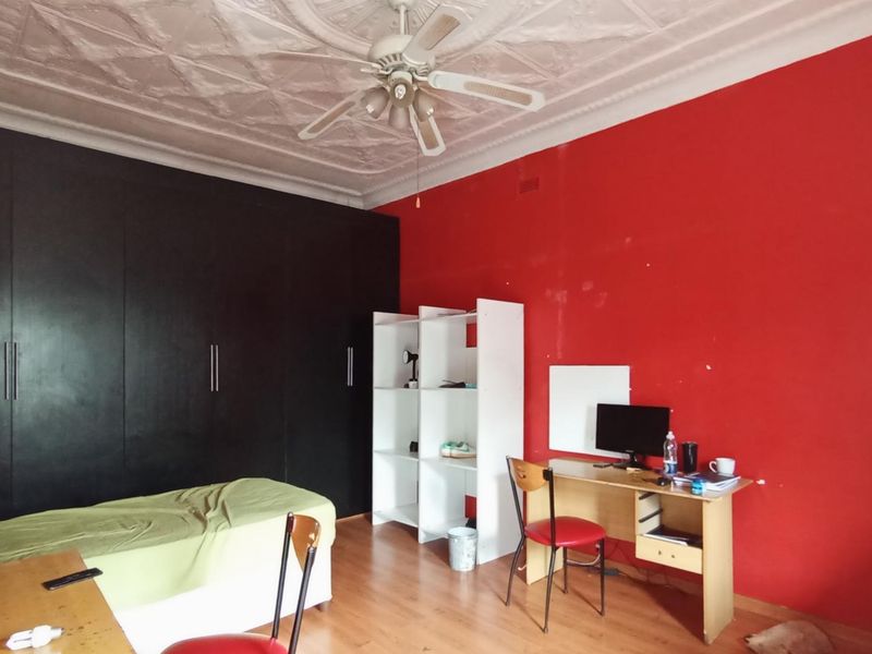 A bedroom featuring built-in cupboards, an ornate ceiling with a fan, and laminate flooring. The room requires cosmetic updates to the wall finishes.