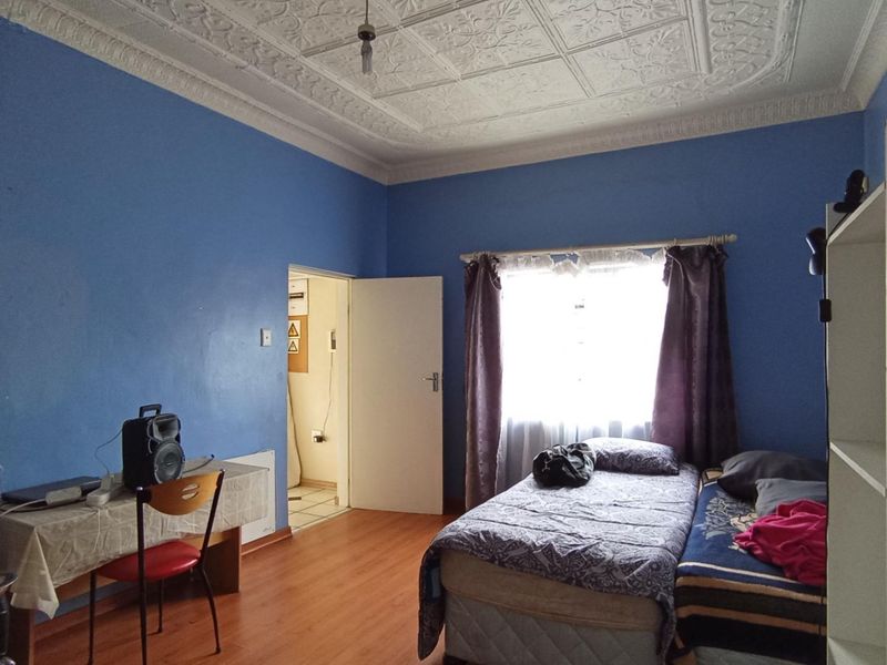 A bedroom featuring a distinctive ornate pressed metal ceiling, laminate flooring, and classic cornicing, offering a solid foundation for renovation.