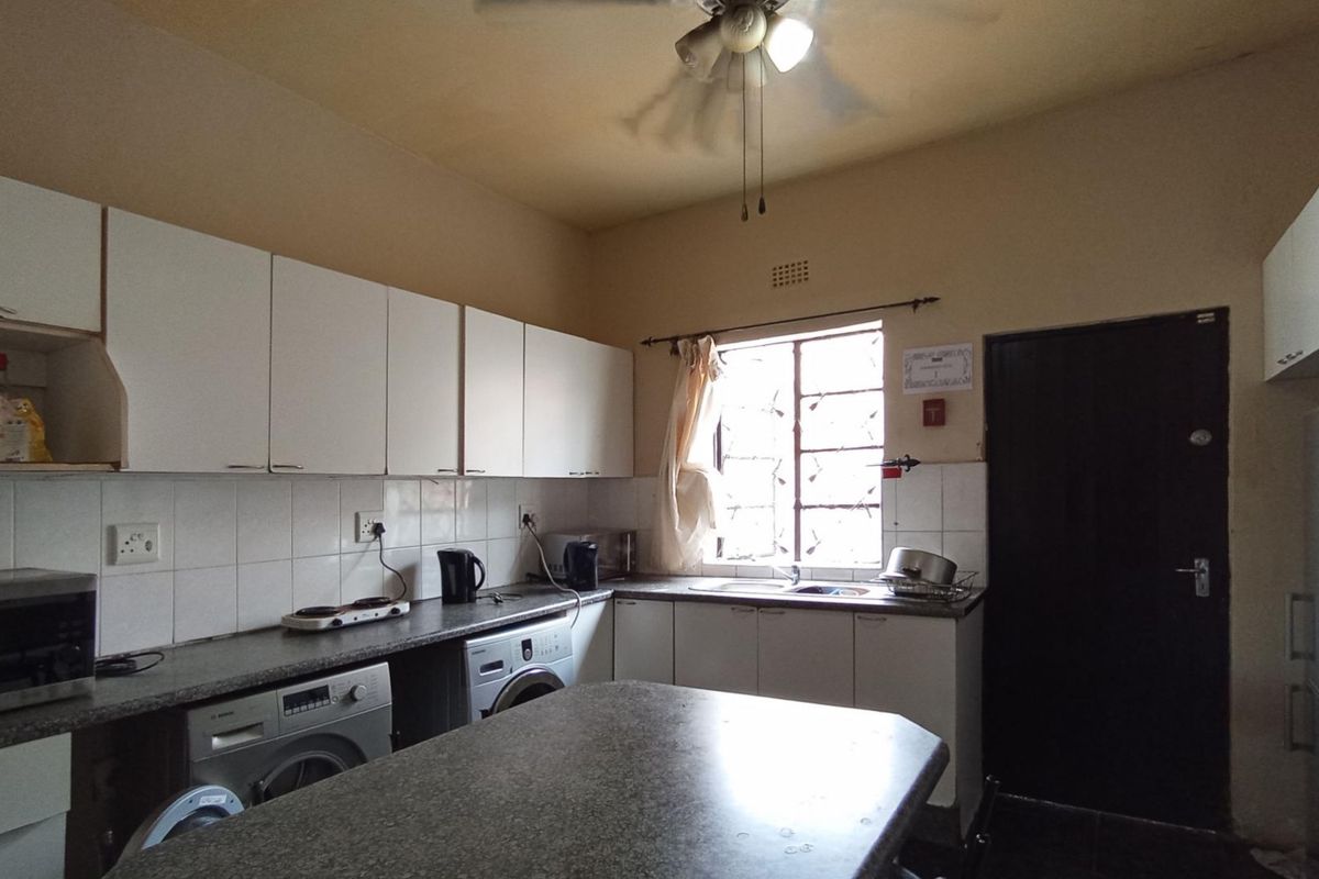 A functional kitchen featuring built-in cabinetry, laminate countertops, tiled backsplash, and integrated plumbing for laundry appliances, with a security gate at the rear entrance.