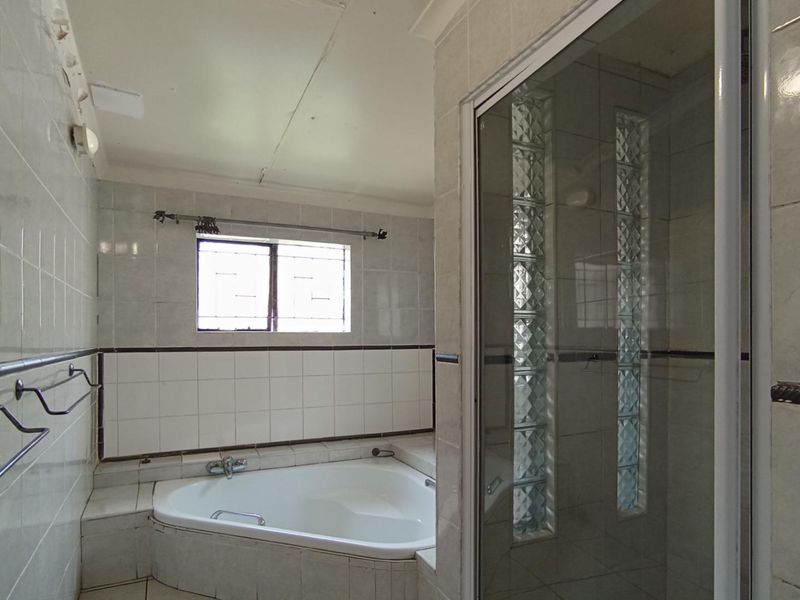A dated bathroom featuring a corner bathtub, a glass-enclosed shower with glass block accents, and full-height ceramic wall tiling.