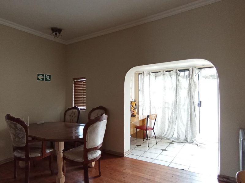 Dining room featuring warm wooden flooring, an elegant arched doorway leading to a tiled sunroom area, and classic ceiling cornices.