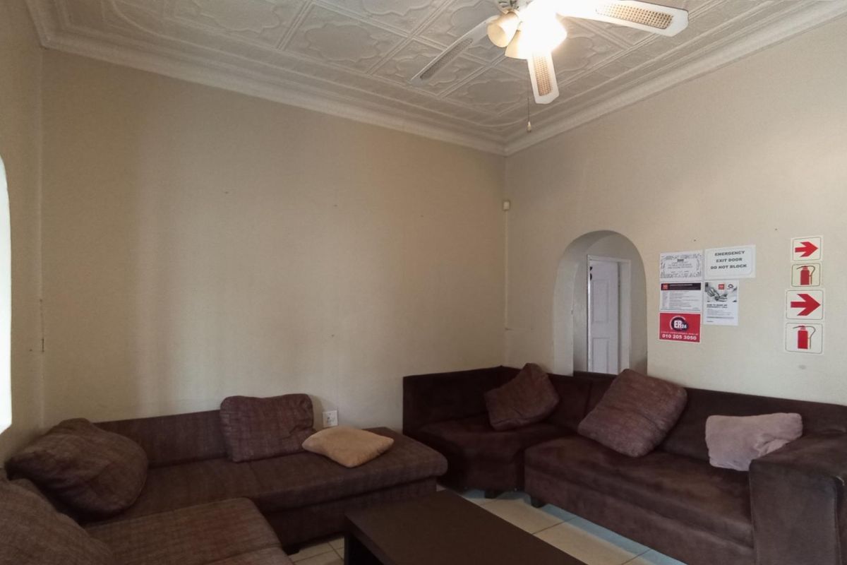 A living room featuring an ornate pressed metal ceiling, ceiling fan, and arched architectural details, currently used as a communal or waiting area.
