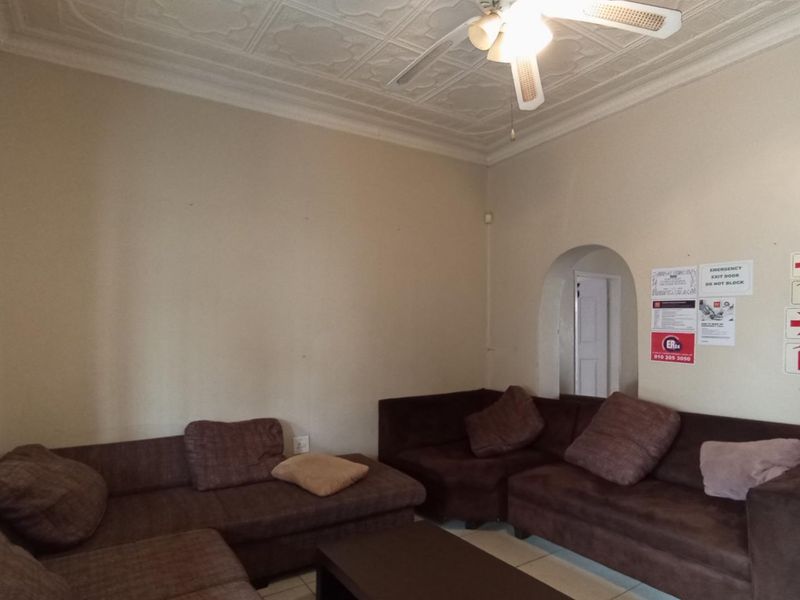 A living room featuring an ornate pressed metal ceiling, ceiling fan, and arched architectural details, currently used as a communal or waiting area.