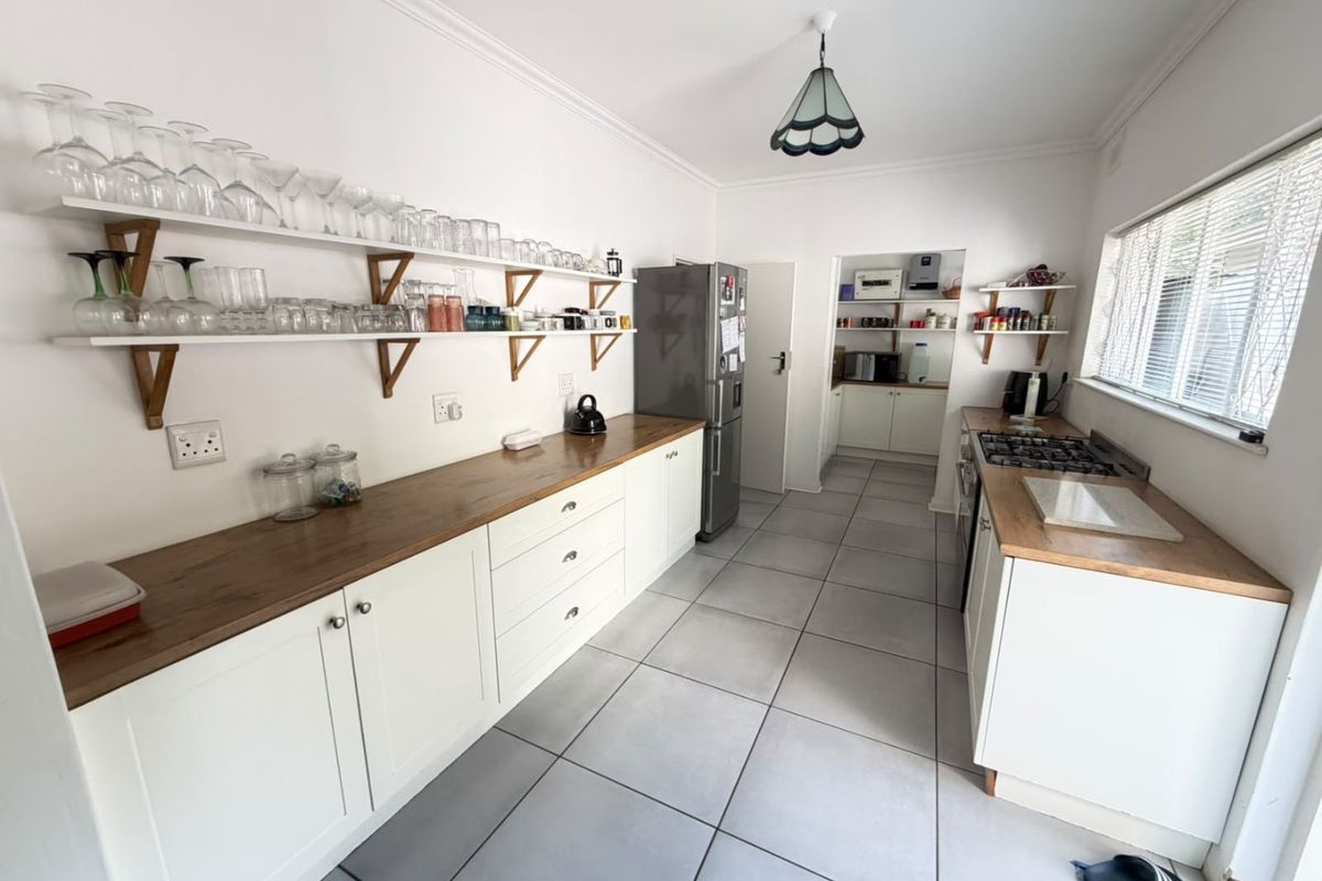 A functional kitchen featuring white cabinetry, wooden countertops, gas hob, and tiled flooring, with an adjoining scullery area for additional storage and prep space.