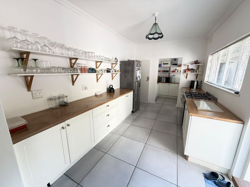 A functional kitchen featuring white cabinetry, wooden countertops, gas hob, and tiled flooring, with an adjoining scullery area for additional storage and prep space.