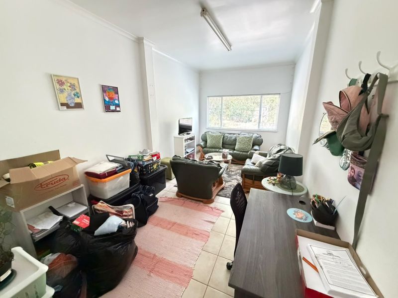 A functional living room featuring tiled flooring and a large window with security bars, offering a versatile space for relaxation.
