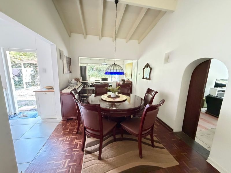 A dining room featuring classic parquet flooring, exposed ceiling beams, and an arched doorway leading to adjacent living spaces.