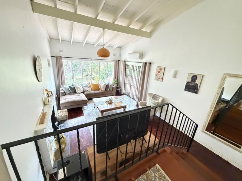 Spacious living room featuring high exposed beam ceilings, parquet flooring, a fireplace, and large windows providing ample natural light and garden views.