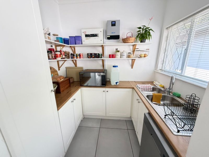 A functional scullery featuring white cabinetry, timber countertops, a double stainless steel sink, and open shelving for convenient storage and prep space.