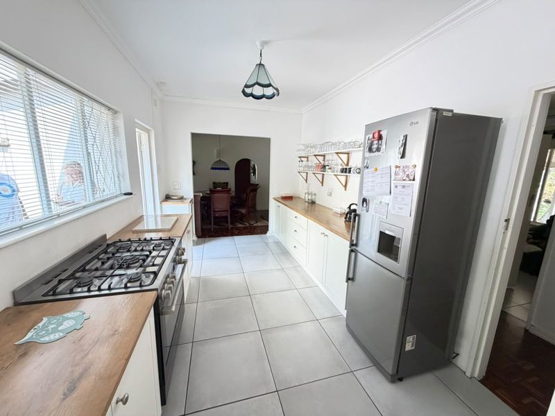 A functional kitchen featuring wooden countertops, built-in cabinetry, a gas hob, and tiled flooring, with an open flow into the adjacent dining area.