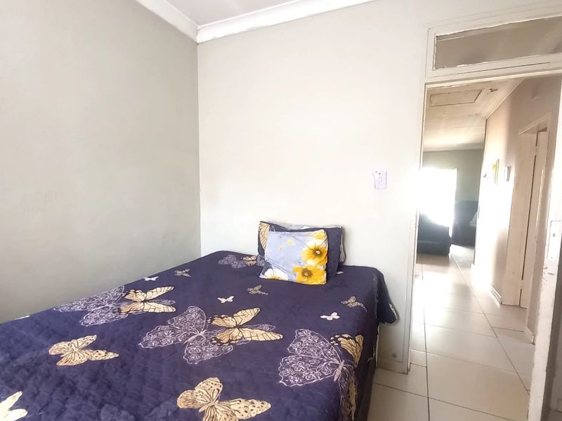 A compact bedroom featuring tiled flooring and a transom window above the doorway, leading into a connecting hallway.