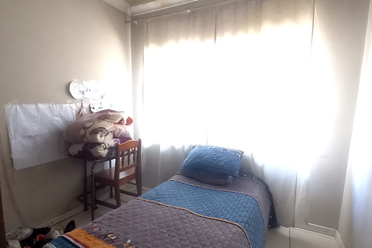 A compact bedroom featuring tiled flooring and a window with natural light. The ceiling shows visible signs of water damage and requires maintenance.