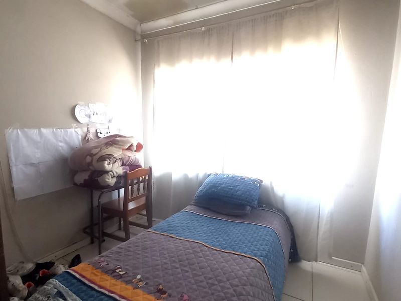 A compact bedroom featuring tiled flooring and a window with natural light. The ceiling shows visible signs of water damage and requires maintenance.