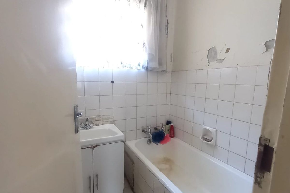 A compact bathroom featuring a built-in vanity and bathtub, requiring cosmetic updates and repairs to wall finishes and cabinetry.
