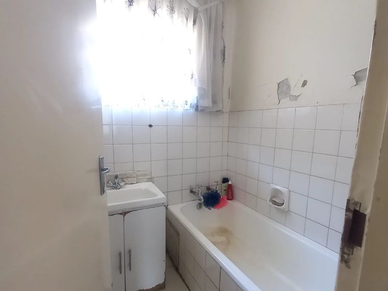 A compact bathroom featuring a built-in vanity and bathtub, requiring cosmetic updates and repairs to wall finishes and cabinetry.