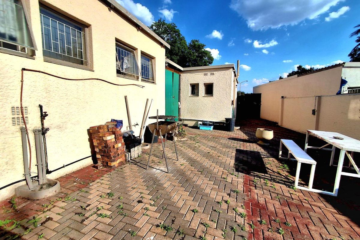 A paved rear courtyard area featuring exterior walls with security bars and an outdoor water tap, requiring some maintenance to the paving.