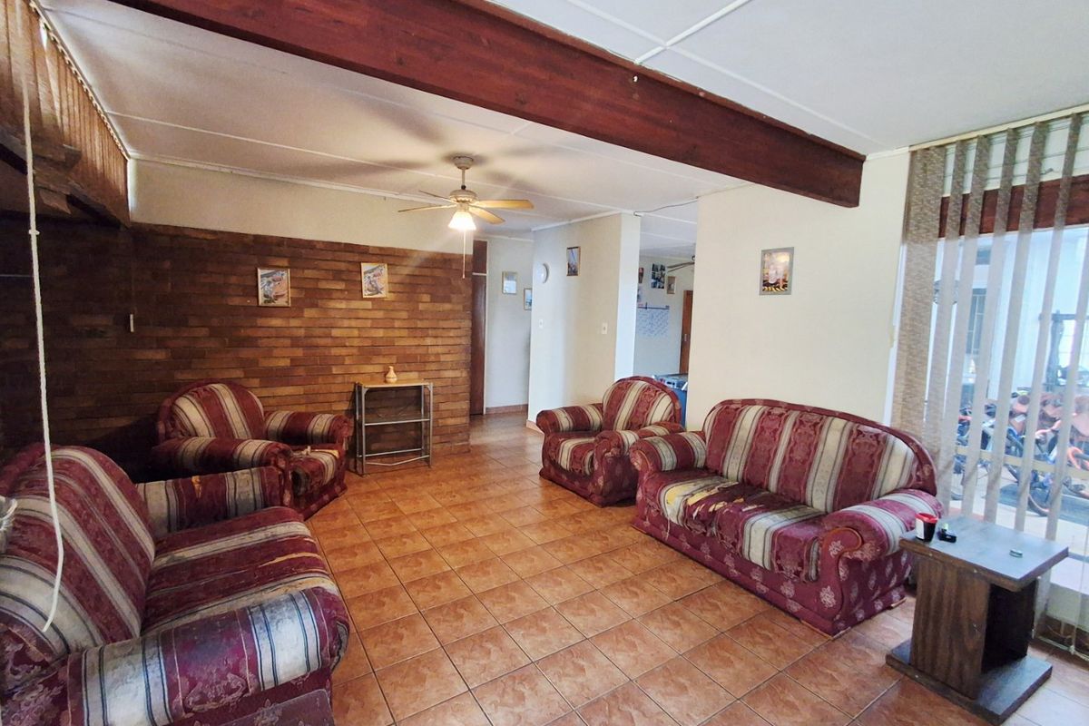 Spacious living room featuring a rustic brick accent wall, exposed timber ceiling beam, and durable ceramic floor tiles.