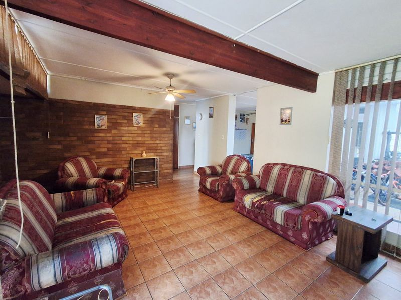 Spacious living room featuring a rustic brick accent wall, exposed timber ceiling beam, and durable ceramic floor tiles.