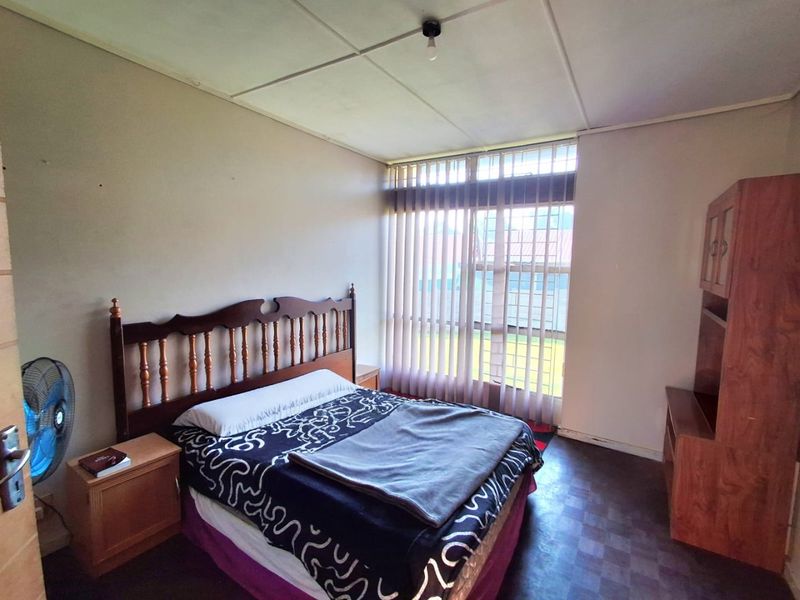 A bedroom featuring tiled flooring, vertical blinds, and a ceiling light fixture, requiring cosmetic updates to improve its overall condition.