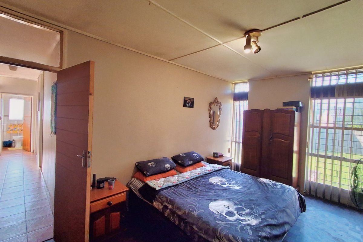 A bedroom featuring security bars on windows and ceiling tiles, with an adjacent hallway view showing tiled flooring.