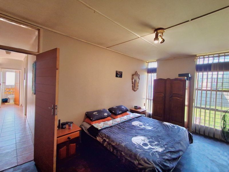 A bedroom featuring security bars on windows and ceiling tiles, with an adjacent hallway view showing tiled flooring.