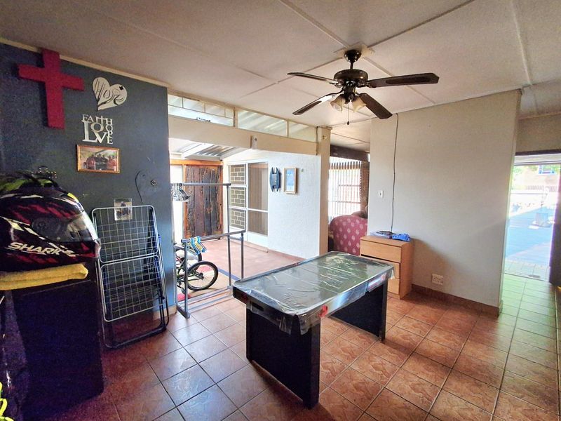 A living area featuring tiled flooring, a ceiling fan, and access to an adjacent patio space through sliding doors.