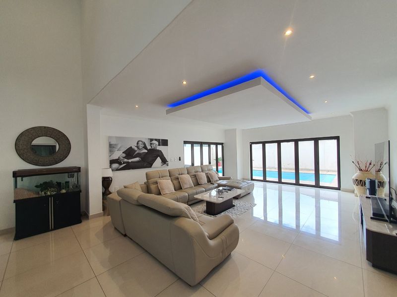 Spacious living room featuring high ceilings with modern LED recessed lighting, large format floor tiles, and bi-fold doors opening to a pool area.
