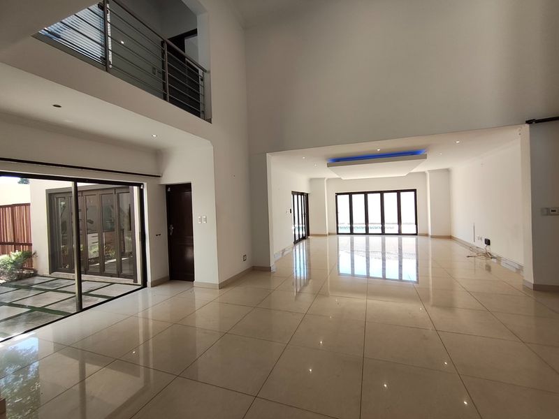 Spacious double-volume living area featuring polished porcelain tiles, modern bulkhead lighting, and large aluminium doors providing seamless access to the outdoor space.