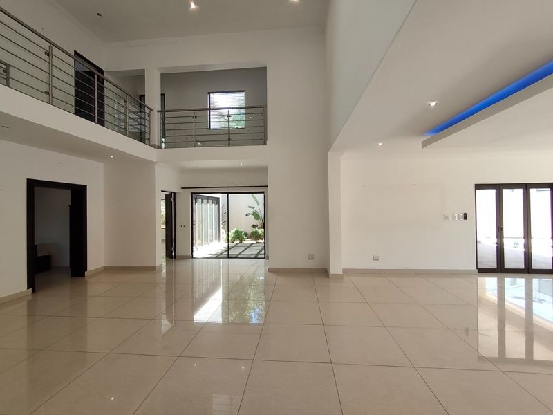 Spacious double-volume living area featuring polished porcelain tiles, modern stainless steel balustrades, and integrated cove lighting with seamless access to the outdoor area.