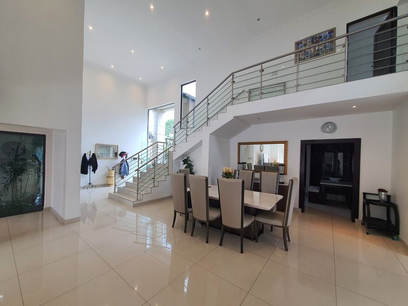 Spacious dining area featuring high ceilings, polished tile flooring, and a modern staircase with stainless steel balustrades leading to a mezzanine level.
