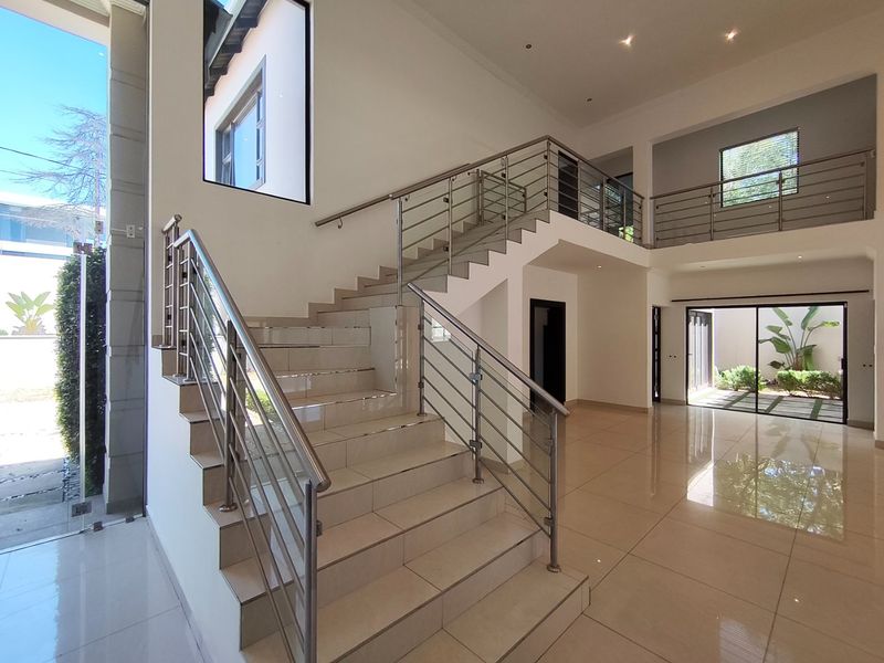 Spacious double-volume entrance hall featuring a modern tiled staircase with stainless steel and glass balustrades, complemented by polished porcelain flooring and abundant natural light.