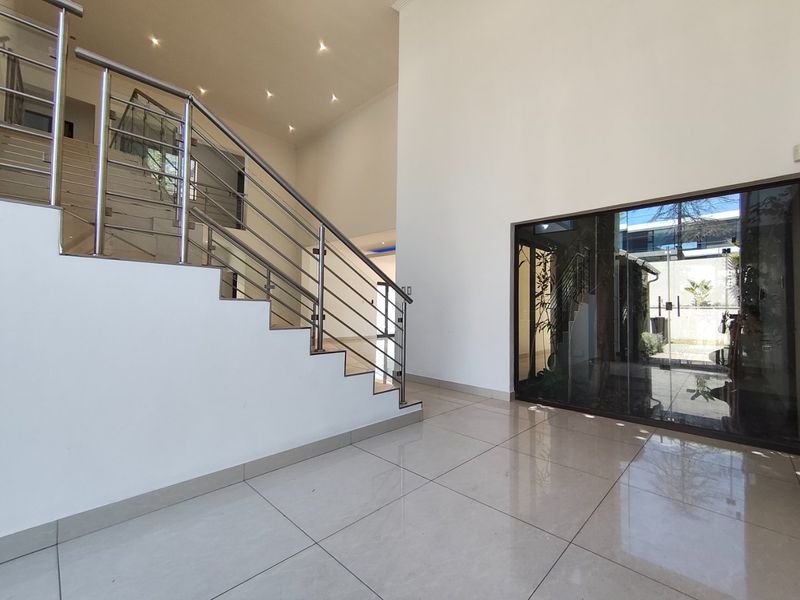 Spacious entrance hall featuring high ceilings, polished tiled flooring, and a modern stainless steel staircase railing with a large glass feature window.