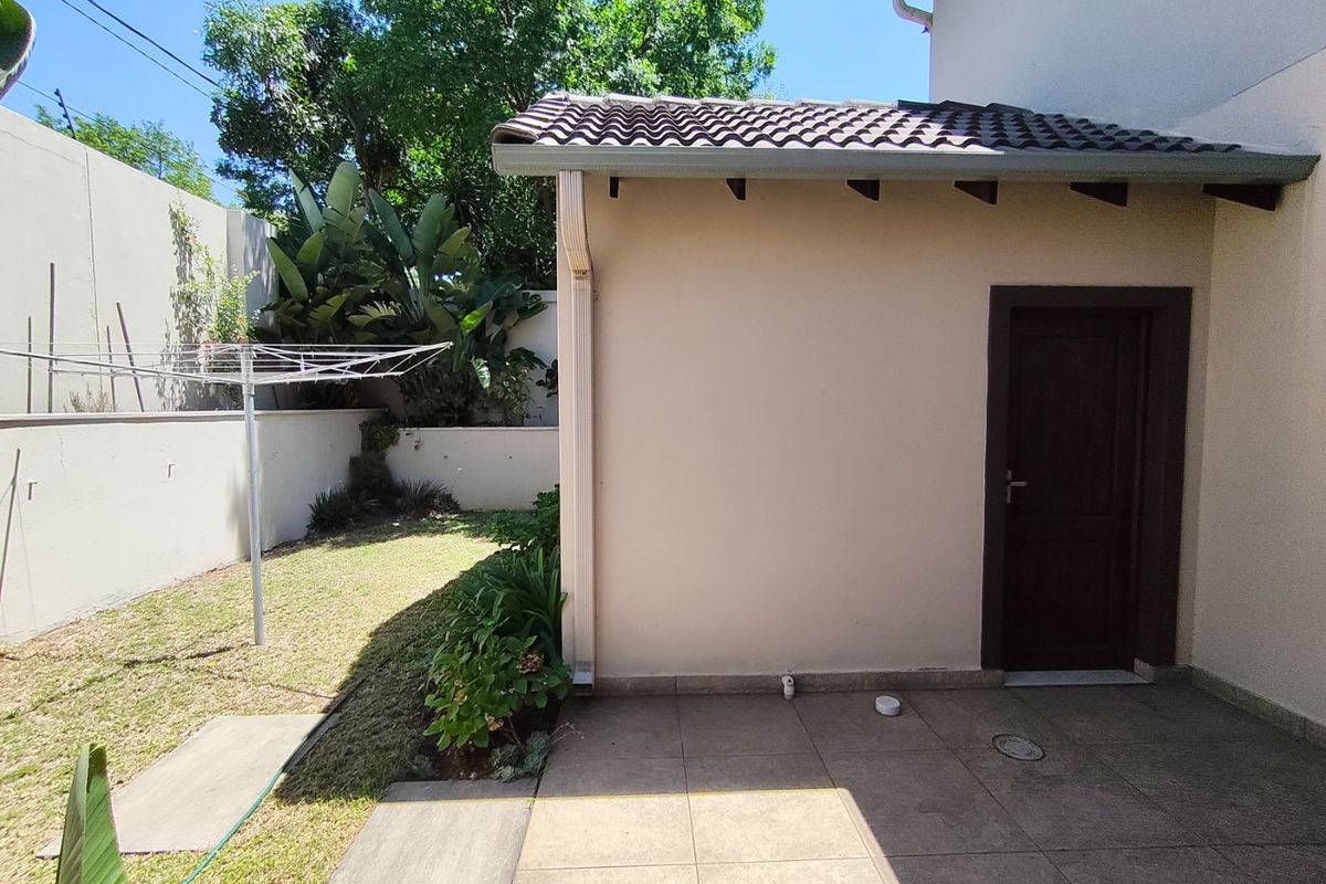 A view of the rear exterior featuring a tiled patio area, a solid external door, and a small garden space with boundary walling.