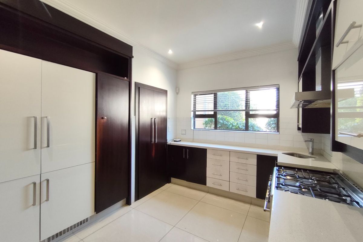 Modern kitchen featuring dark and light cabinetry, stone countertops, gas hob, extractor fan, and tiled flooring with ample storage space.