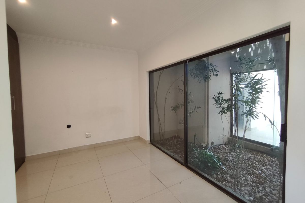 A bright, empty bedroom featuring tiled floors, built-in cupboards, and large sliding glass doors that open onto a private internal courtyard.