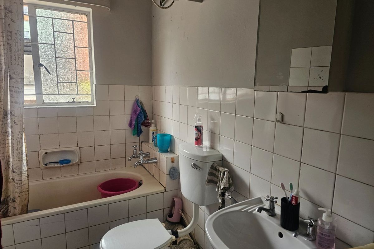 A functional bathroom featuring a bathtub, pedestal basin, and toilet with classic white wall tiling and a window for natural light.