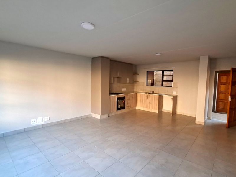 An open-plan living and kitchen area featuring neutral tiled flooring, modern built-in cabinetry, and a functional kitchen layout with integrated appliances.