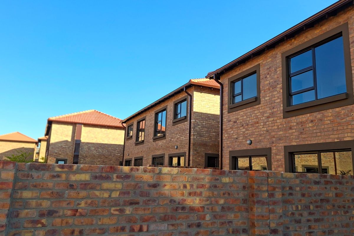 Exterior view of a modern townhouse complex featuring face brick construction, tiled roofing, and dark aluminium window frames.