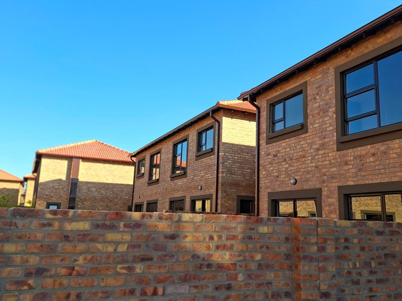 Exterior view of a modern townhouse complex featuring face brick construction, tiled roofing, and dark aluminium window frames.