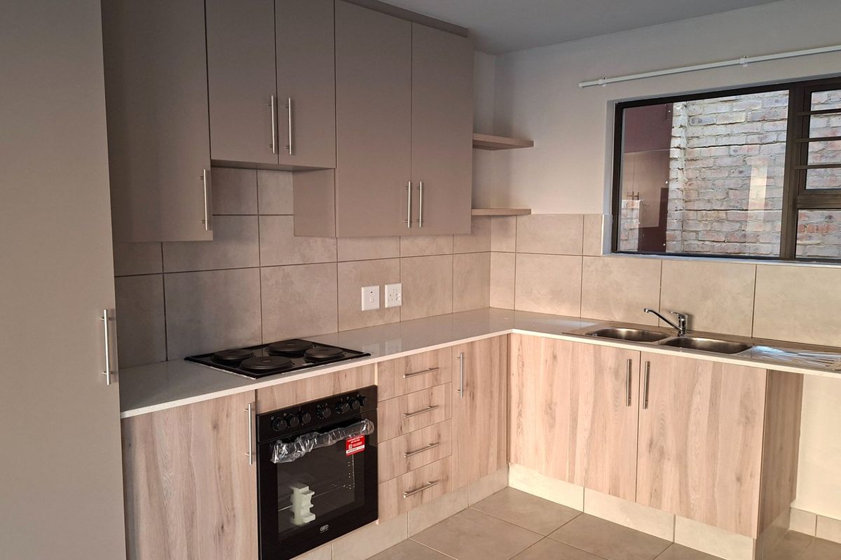Modern kitchen featuring light wood-grain cabinetry, stone countertops, a built-in oven with electric hob, and a double bowl sink with tiled backsplash.