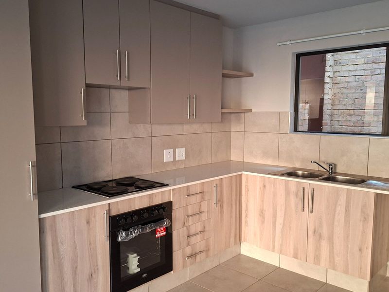 Modern kitchen featuring light wood-grain cabinetry, stone countertops, a built-in oven with electric hob, and a double bowl sink with tiled backsplash.