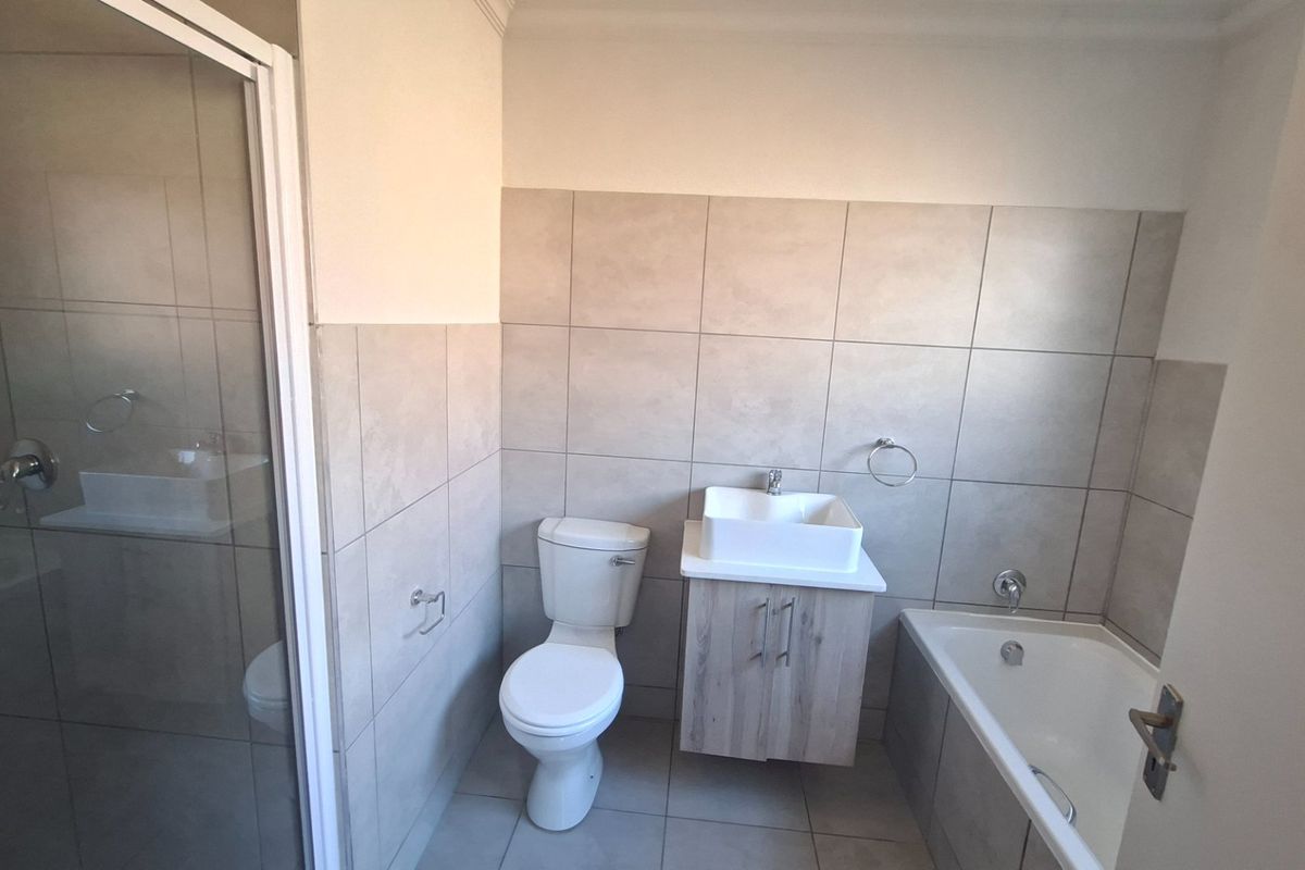 A modern, clean bathroom featuring a shower enclosure, a bathtub, a vanity with a vessel sink, and neutral wall and floor tiling.