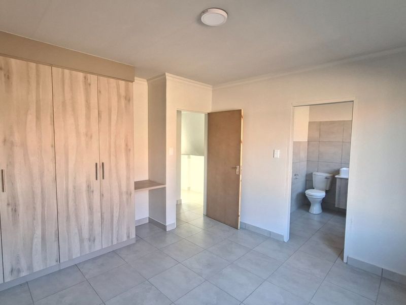 Spacious bedroom featuring modern built-in cupboards, neutral tiled flooring, and direct access to an en-suite bathroom.